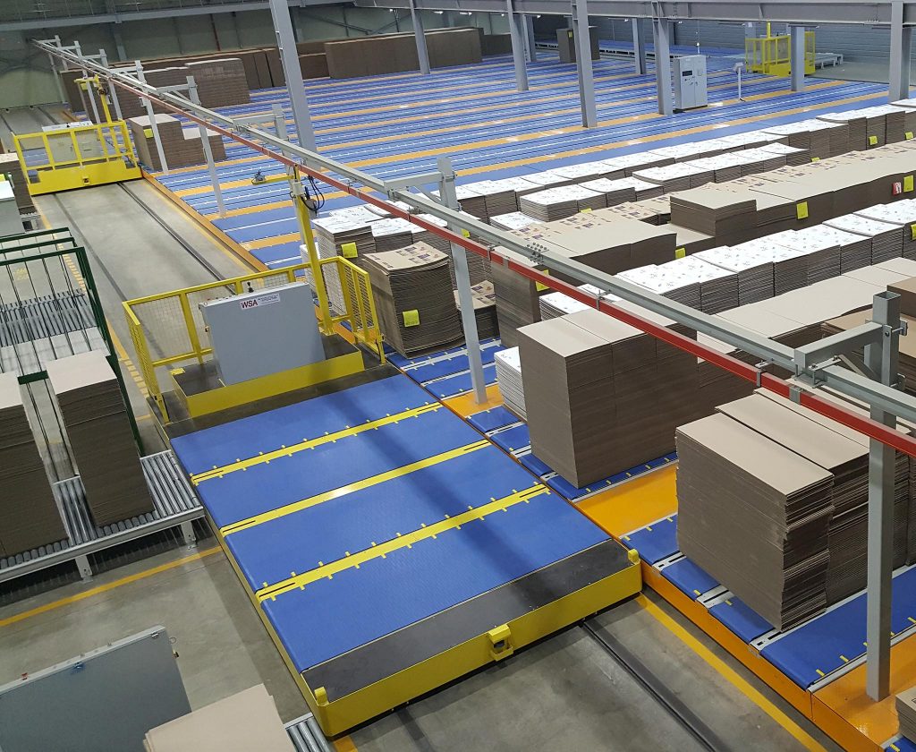 WSA transfer car crossing a plant floor between rows of stacked corrugated board