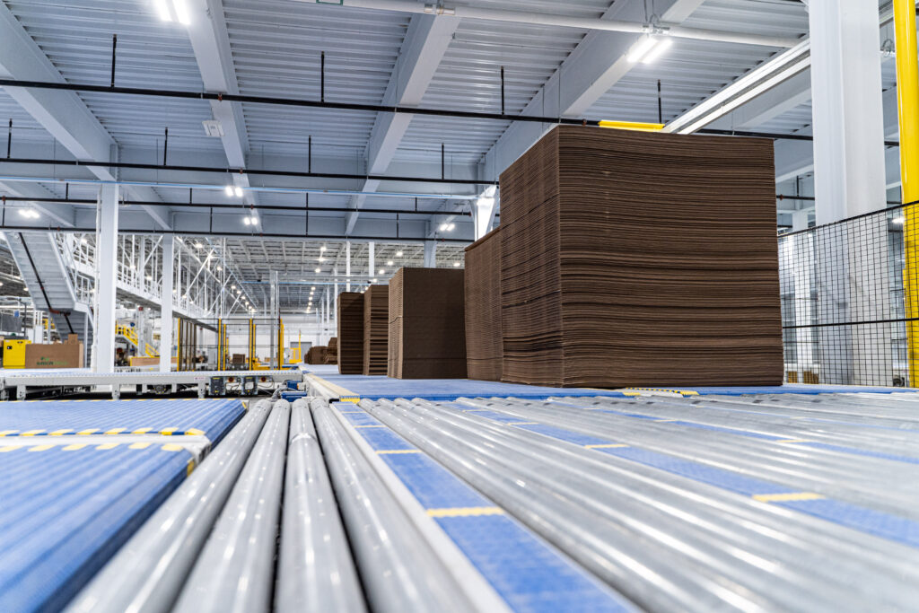Blue modular plastic belt and roller conveyors carrying stacks of corrugated board through a plant