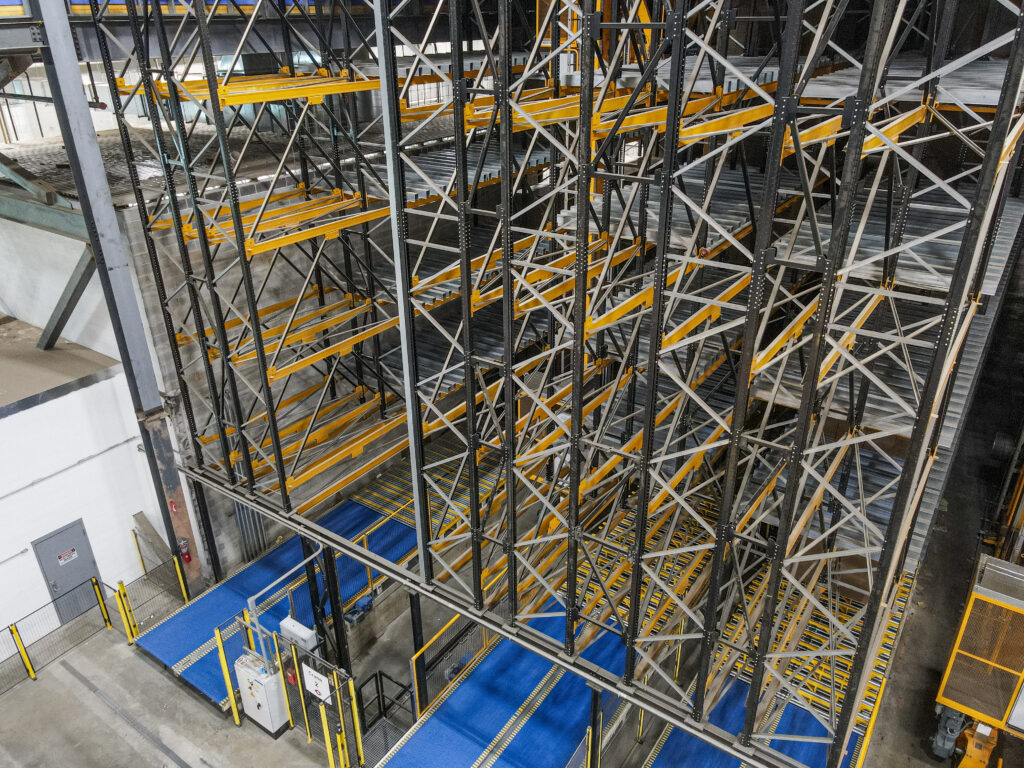 Multi-level vertical rack storage system with blue conveyors feeding it at floor level