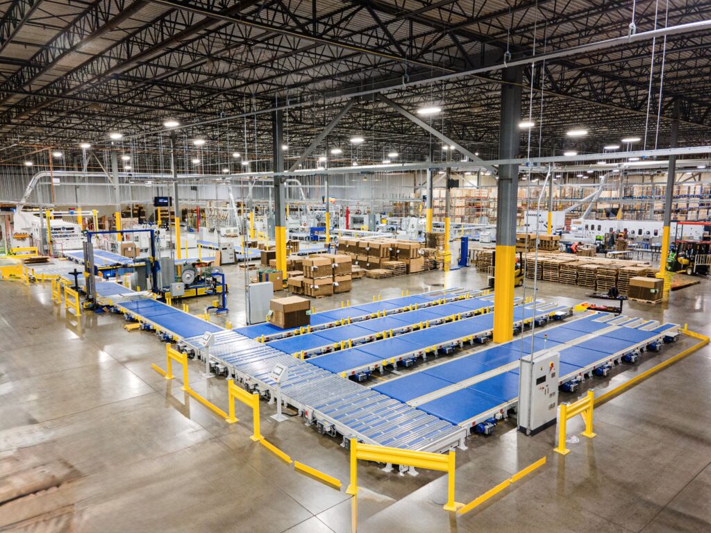 Overhead view of a plant floor with rows of blue belt conveyors and yellow guarding, feeding a strapping line